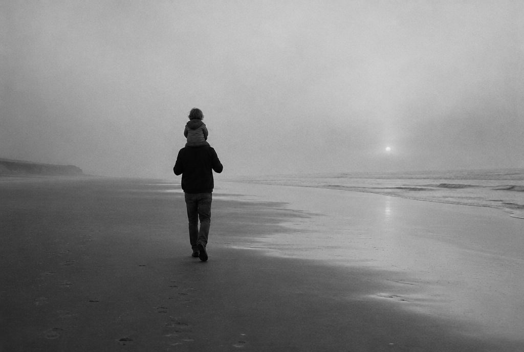 Un hombre camina por la playa al amanecer con un niño en hombros